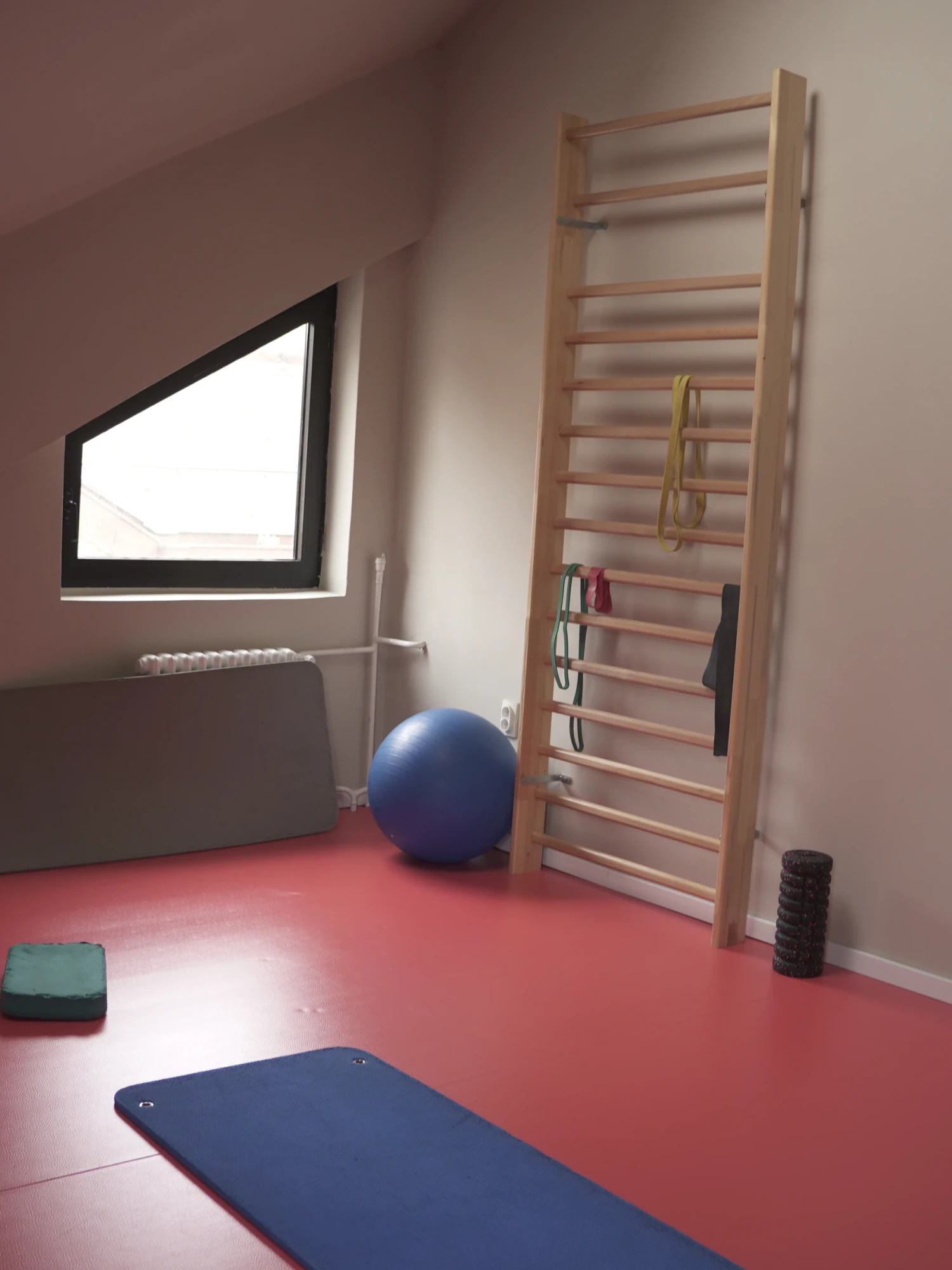 Sala za individualni rad u Advance Fitness Centru, pod kosim krovom — švedske lestvice sa elastičnim trakama, lopta za vežbanje, valjak i strunjače na podu.