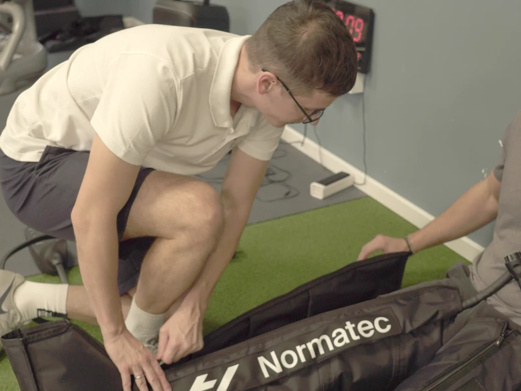 Trener Advance Fitness Centra postavlja Normatec kompresione čizme na noge sportiste pre programa oporavka.